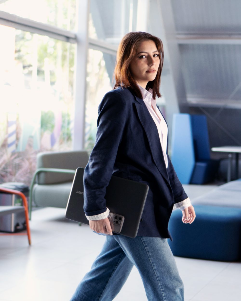 Dheniffer Vieira, fundadora da DHN Business & Brand, caminhando com notebook em escritório moderno