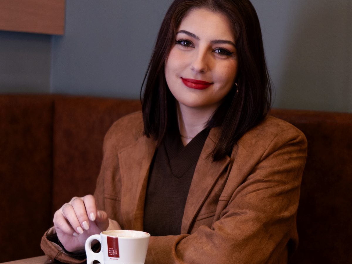 Dheniffer Vieira sorrindo em um café, com xícara nas mãos